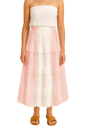 A female model posing in profile while wearing an off-white peach tiered maxi skirt. The skirt features a smocked waistband and multiple ruffled tiers, displayed against a clean white backdrop.